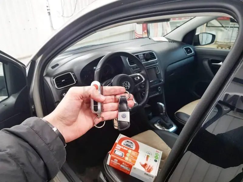 Рука с брелоком StarLine в салоне Volkswagen, на сиденье — упаковка StarLine